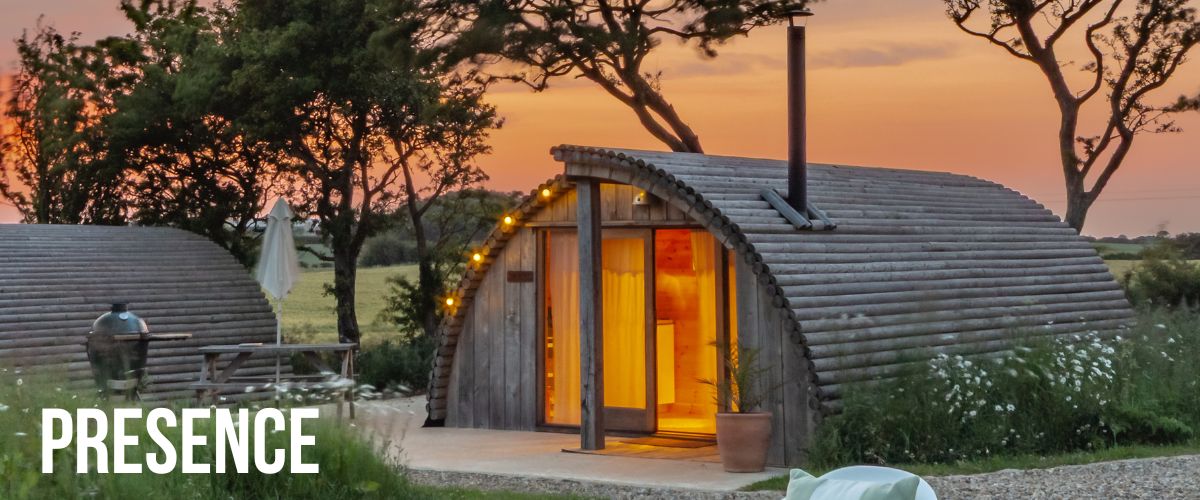 Presence premium glamping pod at sunset with XL hot tub, Yorkshire countryside views, wood-burning stove, and romantic lighting